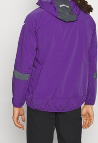 Giacca leggera viola con cappuccio grigio, orlo elastico e dettagli riflettenti sulle maniche. Il tessuto sembra liscio e resistente all'acqua.