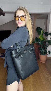 Czarna skórzana torba tote z podwójnymi uchwytami, z dekoracyjnymi elementami i gładką fakturą, ustawiona na neutralnym tle wnętrza.