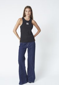 Black tank top with a fitted design and round neckline, featuring white logo details. Paired with dark blue wide-leg jeans and contrasting stitching.