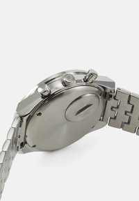 Stainless steel watch with a round case, polished surface, and three pushers. Metal link bracelet with a smooth texture and shiny finish.