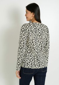 Tops à manches longues en crème avec imprimé léopard noir. Doté d'un col rond et d'une coupe décontractée, fabriqué dans un tissu doux et texturé.
