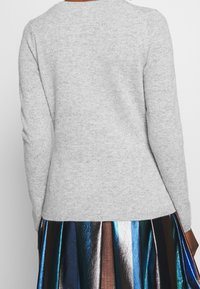Grey knitted sweater with long sleeves and a round neckline, displayed from the back, paired with a metallic pleated skirt.