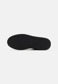 Semelle de chaussure en caoutchouc noir avec un motif en chevrons. Présente une boîte logo rectangulaire avec la marque "AX" au centre. Fini plat et lisse.