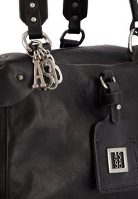 Zwarte leren tas met zilveren AS98-logo op het bijgevoegde label en sleutelhangers die aan de zwarte leren schouderriem met metalen klinknagels hangen.
