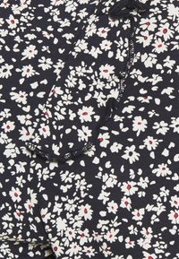 Námořnická látka s malým květinovým vzorem, který obsahuje bílé květy s červenými středy, ozdobená volánovým okrajem na jedné straně.