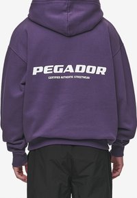Felpa oversized viola in cotone, con logo bianco "PEGADOR" sulla schiena, accompagnato dal testo "CERTIFIED AUTHENTIC STREETWEAR".