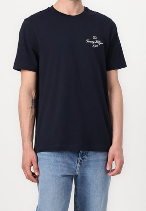 T-shirt en coton bleu marine à manches courtes, col rond, avec le logo "Tommy Hilfiger" brodé sur la poitrine gauche. Design uni.