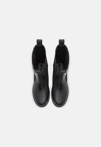 Bottes cheville en cuir noir avec panneaux élastiques sur les côtés, bout arrondi et tirants au talon, présentant une texture lisse et un design minimaliste.
