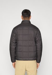 Μαύρο μπουφάν τύπου puffer με σχεδιασμό καπιτονέ και όρθιο γιακά, με μακριά μανίκια και λεία, λαμπερή υφή.