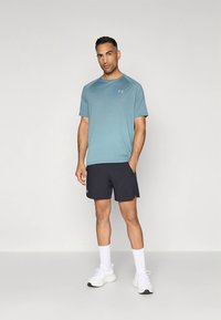 Lys blå sportst-skjorte med horisontale striper, kombinert med mørke shorts. Modellen har på seg hvite joggesko og ankelsokker.