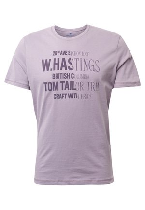 T-shirt en coton violet clair à manches courtes, arborant une typographie variée dans des nuances plus foncées, comprenant des phrases et le nom de la marque affiché de manière bien visible.