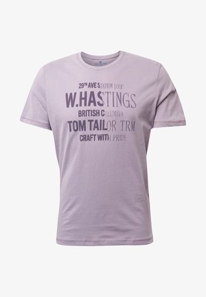 T-shirt in cotone viola chiaro con maniche corte, caratterizzata da una tipografia variata in tonalità più scure, includendo frasi e il nome del marchio in evidenza.