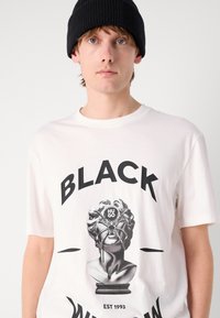 Hvit T-skjorte med korte ermer, med et svart grafisk design av en byste med stropper, og tekst som sier "BLACK" og "HUGO" i fete bokstaver.