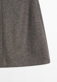 Grauer gewebter Rock mit Fischgrätmuster, in strukturierter Form und glatter Textur. Der Saum ist am Boden leicht ausgestellt.