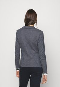 Šedý přiléhavý blazer s límcem, dlouhými rukávy a černobílými proužkovanými manžetami. Hladká textura a přizpůsobený design.