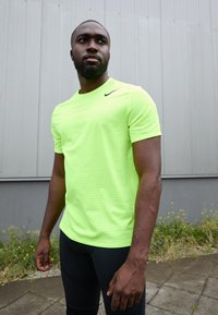 Neonowy żółty T-shirt sportowy z okrągłym dekoltem i krótkimi rękawami, z małym czarnym logo, w połączeniu z czarnymi dopasowanymi legginsami.