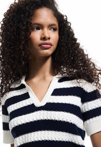 Top a righe blu navy e bianco in maglia con scollo a V e maniche corte. Presenta fasce testurizzate e un design casual e leggero.