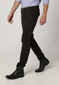 Schwarze, schmal geschnittene Baumwollhosen mit glatter Textur, Gürtelschlaufen und seitlichen Taschen, getragen mit schwarzen Schnürstiefeln.