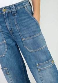 Pantalons cargo en denim bleu clair avec de nombreuses grandes poches, des accents en métal doré et une coupe décontractée avec une taille haute.
