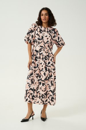 Abito midi floreale in delicate tonalità di rosa, nero e pesca. Presenta maniche a sbuffo, scollo tondo e una gonna a balze. Indossato con tacchi neri.