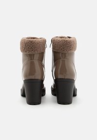 Brune patentlæder ankelstøvler med en hyggelig brun shearling-kant og en kraftig sort hæl, der har en lynlåsdetaile på siden.