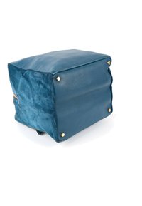 Sac à main en cuir et daim bleu montré par le dessous avec quatre pieds en métal doré sur fond blanc.