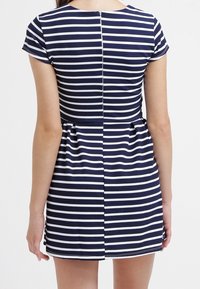 Mekko, jossa on tummansinisiä ja valkoisia raitoja, lyhyet hihat, istuva vartalo ja liehuva hame. Varustettu takaketjulla ja sileällä pinnalla.