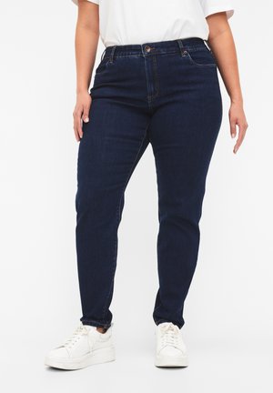 Dunkelblaue Jeans mit einem taillierten Design, Fünf-Taschen-Stil und kontrastierendem Nähen. Kombiniert mit weißen Sneakers.