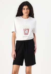 Fehér póló popcorn grafikával piros és fehér színekben, "ATTITŰD" felirattal. Fekete, zsinóros rövidnadrággal párosítva. Simább szövet, laza fazon.