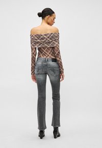 Μπλούζα με καρό μοτίβο σε γήινα χρώματα και ανοιχτούς ώμους, συνδυασμένη με γκρι τζιν στενής γραμμής. Σημαντικές λεπτομέρειες είναι οι πίσω τσέπες και η μαύρη ετικέτα.