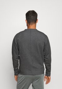 Sweat-shirt gris foncé en tissu doux ; présente un col rond, des manches longues et un ourlet côtelé avec un détail de couture simple.