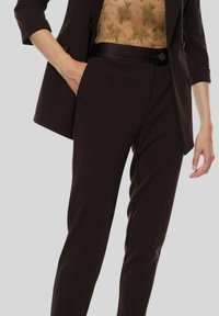 Pantaloni marroni su misura con una texture liscia, a vestibilità slim e tasche laterali. Abbinati a un top trasparente con un motivo sottile e una giacca camicia.