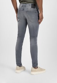 Hellgraue, schmal geschnittene Jeans aus Denim mit Gesäßtaschen und einem schwarzen Lederpatch an der Taille. Kombiniert mit beigen Sneakers.
