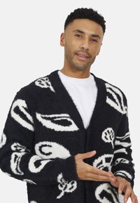 Zwart-witte fluffy cardigan met abstracte patronen, voorzien van een diepe V-hals, lange mouwen en een ontspannen pasvorm. Gelaagd oppervlak.