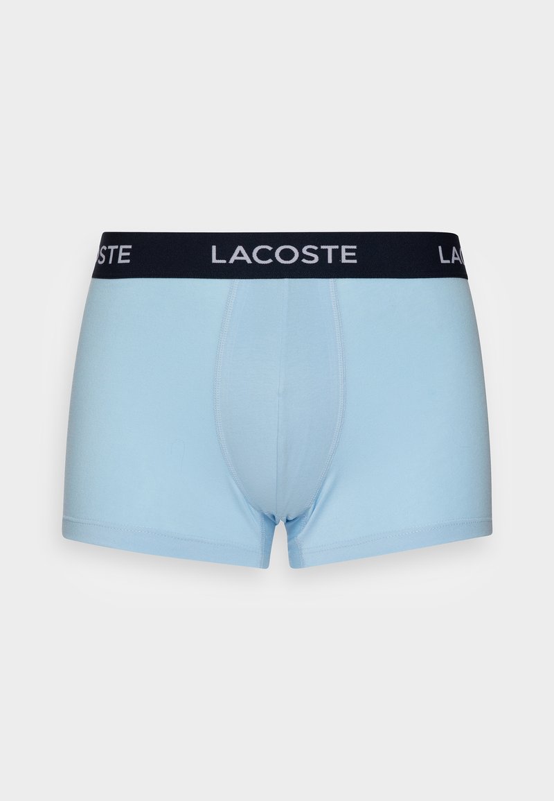 Lichtblauwe boxershorts met een zwarte elastische tailleband met het witte "LACOSTE" logo. Glad stof, aansluitend ontwerp en korte pijpen.