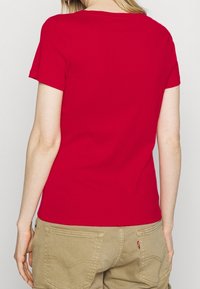Rød t-shirt med korte ærmer lavet af bomuld, med rund hals og glat tekstur. Modellen bærer khaki bukser med baglommer.