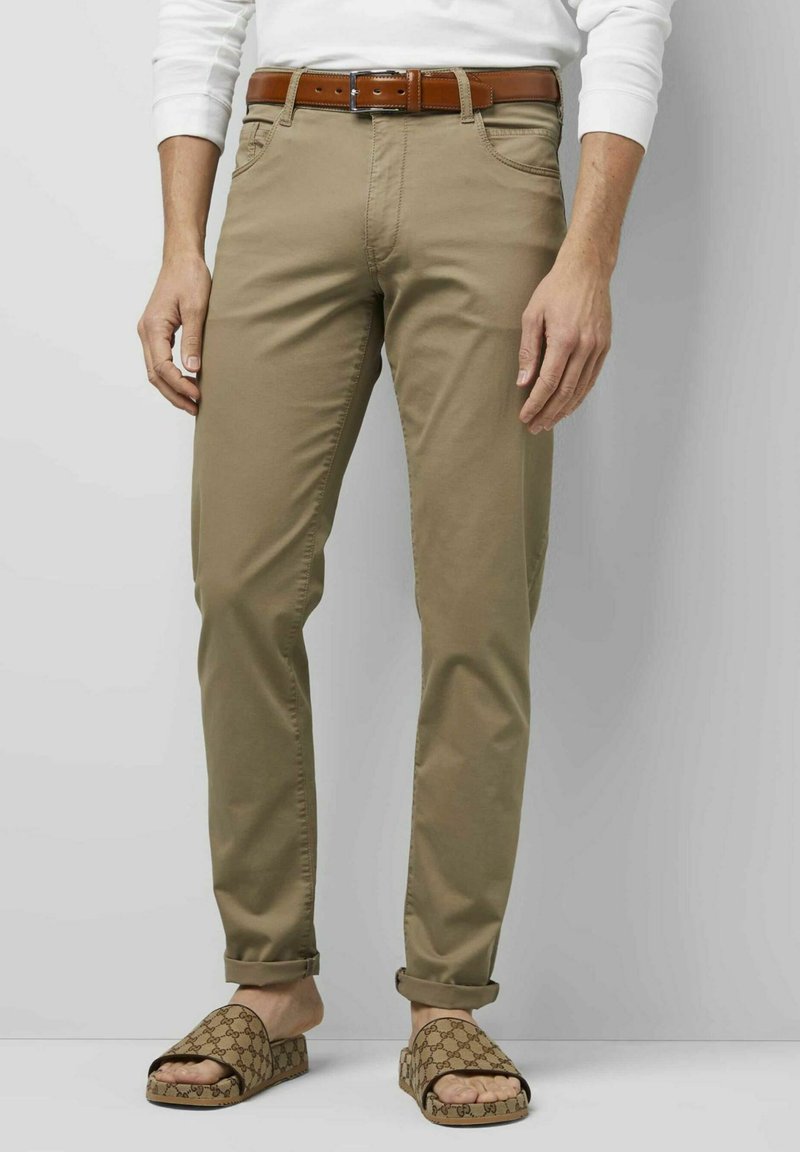 Beige Chinos mit schlanker Passform und umgeschlagenen Bündchen, ausgestattet mit Vorderaschen und einem braunen Ledergürtel. Kombiniert mit gemusterten Rutschsandalen.