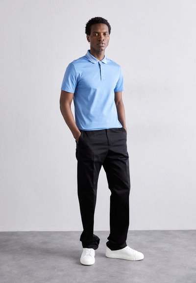 Polo azul claro com mangas curtas e colarinho, combinado com calças pretas e ténis brancos. Design simples, textura suave.