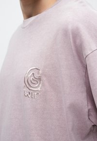 Διχρωμη βαμβακερή μπλούζα σε ανοιχτό μωβ χρώμα με μικρό, κεντημένο λογότυπο σε αντίθετο χρώμα, το οποίο βρίσκεται στην αριστερή πλευρά του στήθους.