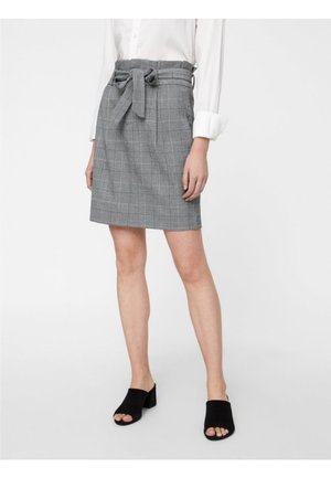Jupe à carreaux grise avec une ceinture à nouer, coupe droite et poches. Associée à des mules noires ouvertes et une chemise blanche à manches longues.