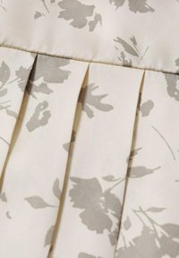 Beige stof med gråt blomstermønster og plisseret design, der har subtil skygge og struktur. Glat overflade, blød at røre ved.