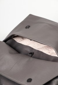 Graue Lederhandtasche mit strukturiertem Finish, ausgestattet mit schwarzem Druckverschluss und einem hellen, gemusterten Innenfutter.