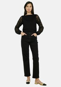 Haut noir à manches longues avec des détails en dentelle, associé à un jean noir taille haute avec une coupe droite et des embellissements subtils.