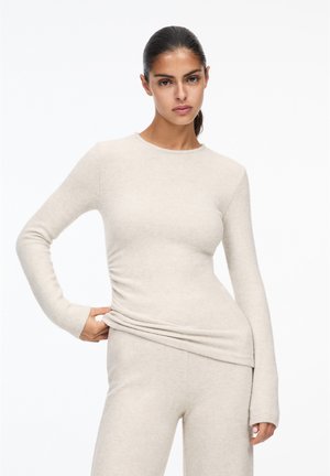 Beige long-sleeve top made of soft fabric, featuring a round neckline and a subtle ruched detail along the side for a fitted look.