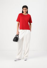 Röd kortärmad t-shirt i kombination med vida vita byxor. En svart strukturerad handväska och vita kanvas skor fulländar outfiten.