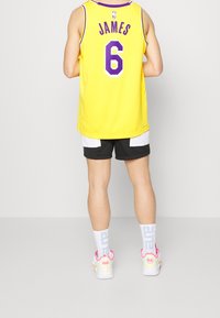 Žlutý basketbalový dres s fialovými detaily a nápisem "JAMES 6" na zádech, doplněný černými kraťasy a barevnými teniskami. Bílé ponožky s nápisem.
