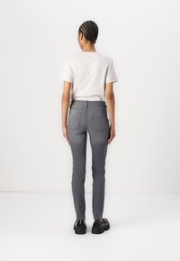 Jeans ajustados grises con una cintura de media altura, que cuentan con bolsillos traseros y una textura de tela suave. Combinados con una camiseta gris claro.