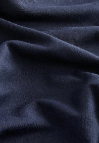 Mörkblå tyg med en slät, texturerad yta som visar mjuka, flödande veck och ett konsekvent vävmönster genom hela ytan.