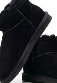 Czarne botki zamszowe z miękką futrzaną wyściółką, płaską gumową podeszwą i kontrastującym przeszyciem. Wykończone teksturowanym detalem na kołnierzu.