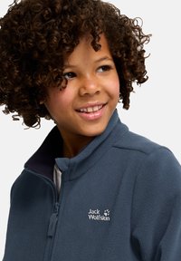 Giacca in fleece blu navy con colletto alto e chiusura con zip; presenta un logo bianco sul lato sinistro del petto; texture morbida e design leggero.